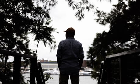 Man standing with his back to the camera, looking out towards a harbour