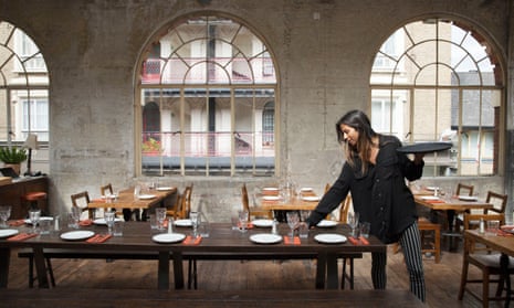 A waitress laying a table in Casa do Frango's dining room with three floor to ceiling arched windows in the background