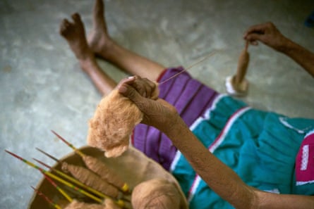 The legs of a woman sitting on the floor next to weaving spindles