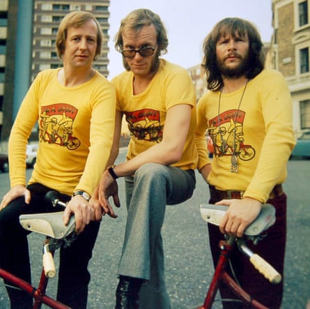 Three men in long-sleeved yellow T-shirts with their hands on a bicycle.