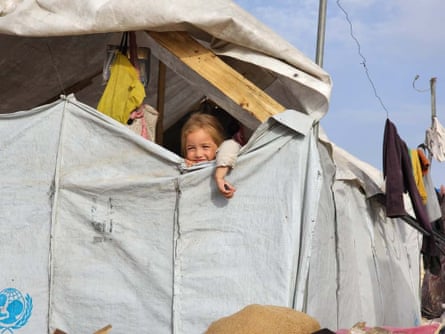 A young girl smiles while looking out through a gap at the top of her tent.