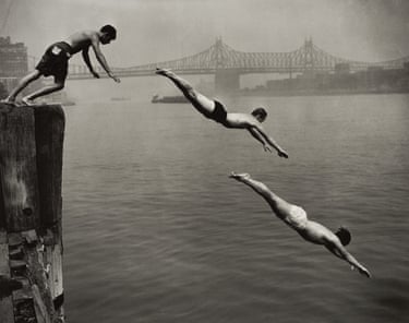Three young men dive in sequence from a wooden pier into the East River, with a bridge visible in the background