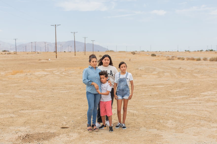 Miriam Juárez stands with her two daughters, her arm around her son on a dusty expanse.