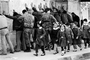 Schoolchildren walk past a group of Palestinian men being searched by Israeli soldiers in the Gaza Strip, November 1986