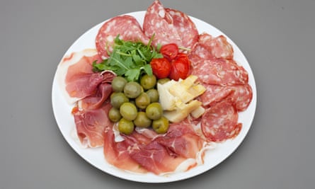 A round white plate of Parma ham and peppercorn salami, with artichoke heart, olives, and rocket in the centre