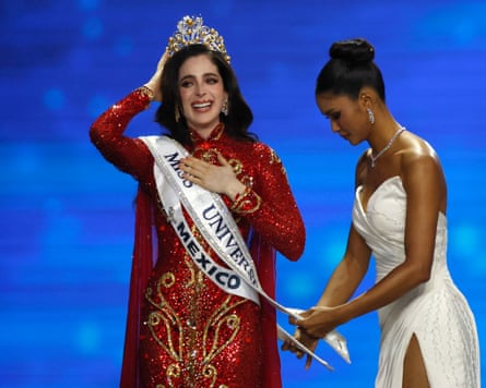 Fátima Bosch wears two sashes, one that says Mexico and one that says Miss Universe. She is wearing an ornate red and gold full length dress and is holding a crown on her head