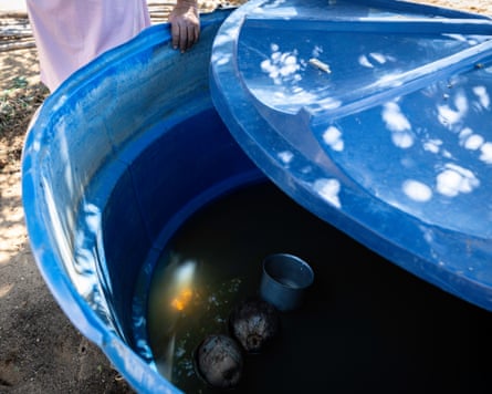 A woman standing by a large plastic water tank with the lid half off