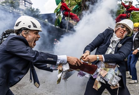 Two activist dressed up as oil executives with their suits covered in money take part in a play-fight