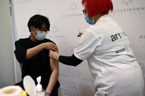A man in a black shirt rolls up his sleeve to get a vaccination.