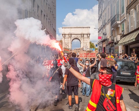 A crowd of protesters, the one nearest the camera holding up a flare, with the Arc de Triomphe in the background