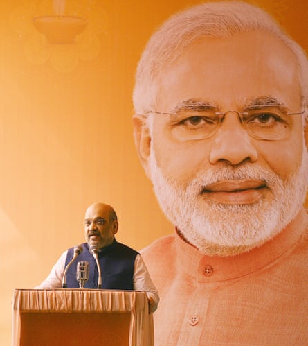 Shah speaks at a podium, while behind him is a huge portrait of Modi.