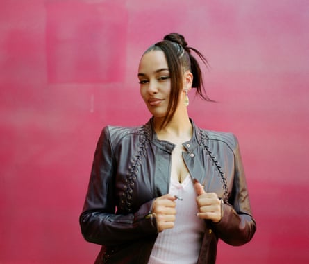 Jorja Smith poses in a black leather jacket against a crimson-coloured wall