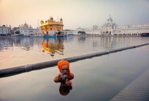 A Sikh pilgrim immersed to his chest in the sacred pool, with the Golden Temple in the background