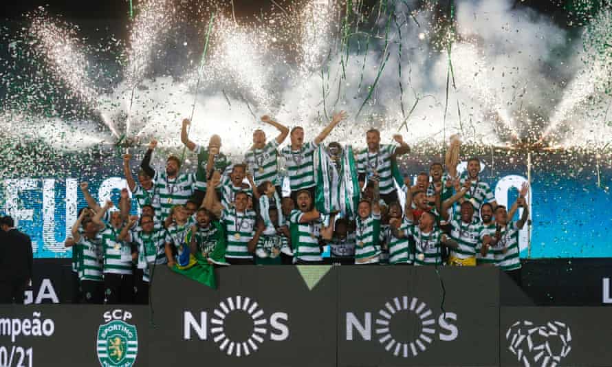 Les joueurs du Sporting célèbrent la victoire de leur première Primeira Liga depuis 2002 en soulevant le trophée tandis que des feux d'artifice se déclenchent en arrière-plan.