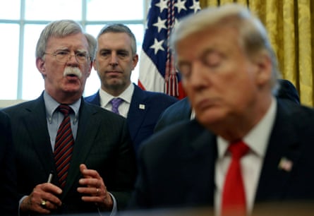 John Bolton at the White House with Trump and another man in the background, all wearing suits
