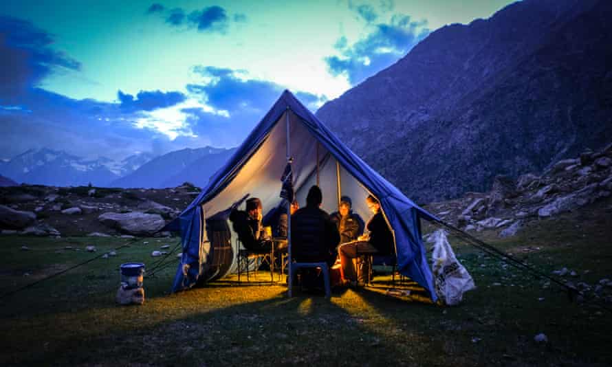 People gathered inside a tent, the front open, mountains behind, as night falls