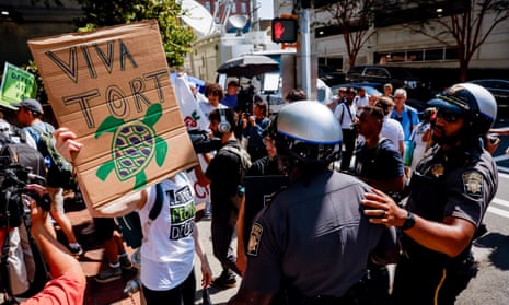 person holds sign that says 'viva tort' with a picture of a turtle, as police stand in front of them