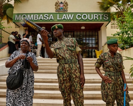 A Kenyan national youth service officer talks to a woman while on guard at the entrance to the Mombasa law courts