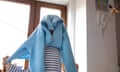 Child (10-11) standing in front of a large window in a bedroom and pulling a blue knitted sweater over her head to get dressed as part of the morning routine.<br>Stock image of a child putting on a jumper