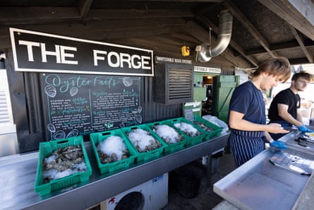 Young people prepare oysters at the Forge with trays of oysters in the background and a menu