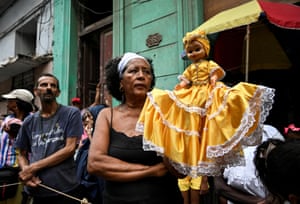 A follower of the Virgin of Charity, Oxun in the Yoruba religion, joins a procession while carrying a doll dressed in an elaborate, lace-fringed dress