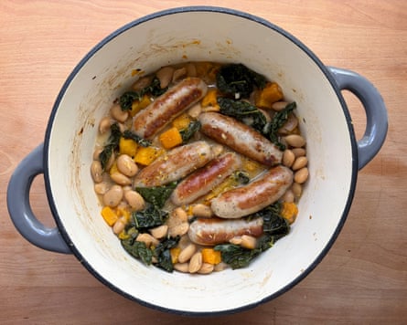Aerial view of a blue and white casserole dish containing sausages with squash and beans.
