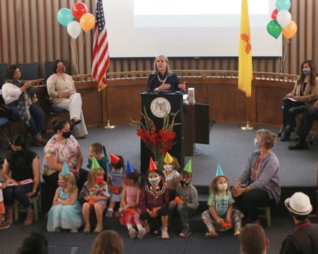 a woman speaks at a podium with children in front