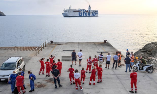 Members of the Italian Red Cross gather on the quay as a quarantine ship makes its way to the port of Lampedusa Island