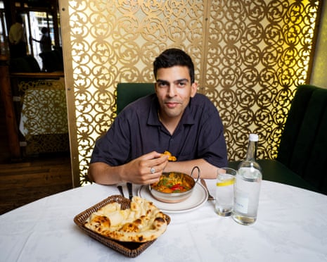Ammar Kalia sits at a large round table covered in a white cloth, eating a balti curry and naan bread