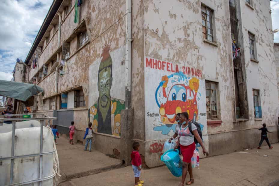 Les gens passent devant des peintures murales peintes par Basil Matsika à Mbare.
