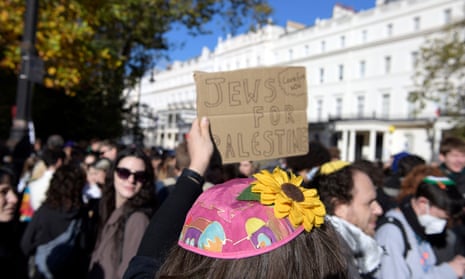 A protestor wearing a kippah with a sunflower on it holds up a placard with ‘Jews for Palestine’ written on it, at the march in London.