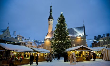 Wooden hut stalls in Tallinn's Town Hall Square with a large xmas tree and the church hall with spire in the background, a bright blue sky and snow on the roofs