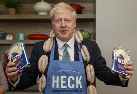 Boris Johnson holds two packets of sausages with a link of sausages around his neck