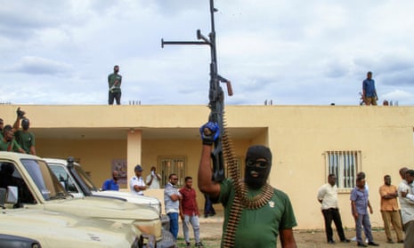 Man wearing balaclava holds an automatic weapon up in air.