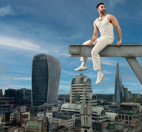 Writer Joe Stone in white vest, trousers and Converse, sitting on a metal girder superimposed against a London landmarks backdrop