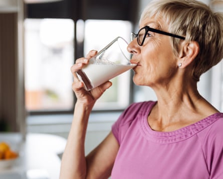 Profile view of a woman drinking fresh milk from a glass in the kitchen