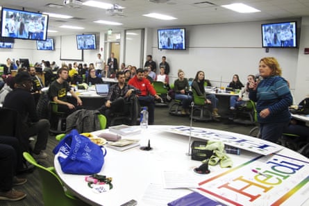 Senator Heidi Heitkamp speaks into a microphone to students in a classroom with TV screens
