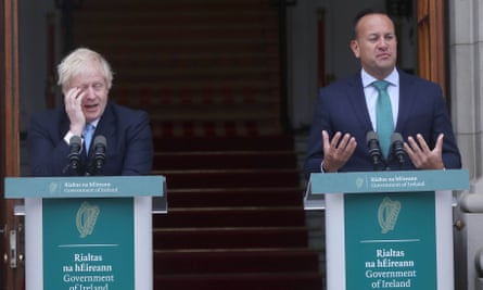 Varadkar speaking at a podium; Boris Johnson stands at an adjacent podium with his head in his hand.