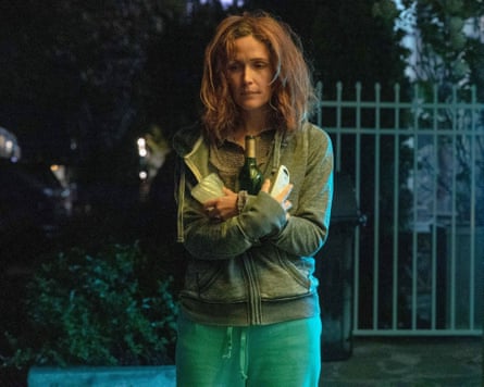 A woman with disheveled hair stands outside with her belongings in her hands