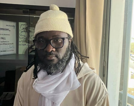 A young African man with glasses and dreadlocks looks at the camera
