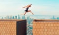 Woman makes dangerous jump over gap between two tall buildings<br>Female with bare feet runs and jumps from one tall building to another. She looks down as she is right a above the gap between the buildings. Big city in the background with skyscapers. Concept of taking a change even though there is a big risk.