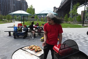 Man cooking food on a barbecue while friends sit on a table awaiting food