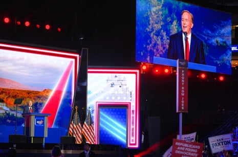 Ken Paxton speaks on stage as his image is displayed on a screen above him