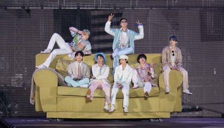 The band, wearing pastels, sit on a giant sofa
