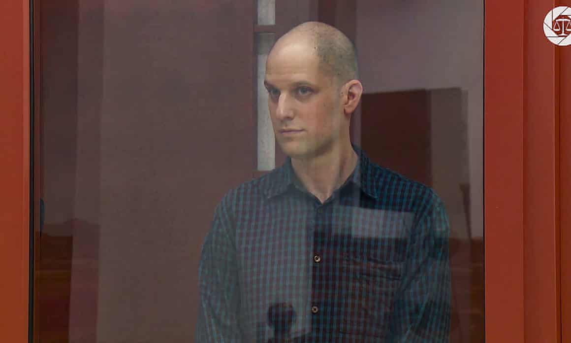 Gershkovich, with his head shaved, stands behind protective glass in a Russian courtroom.
