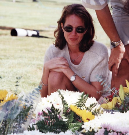 A woman with dark hair and a cream top and sunglasses standing over bouquets of flowers