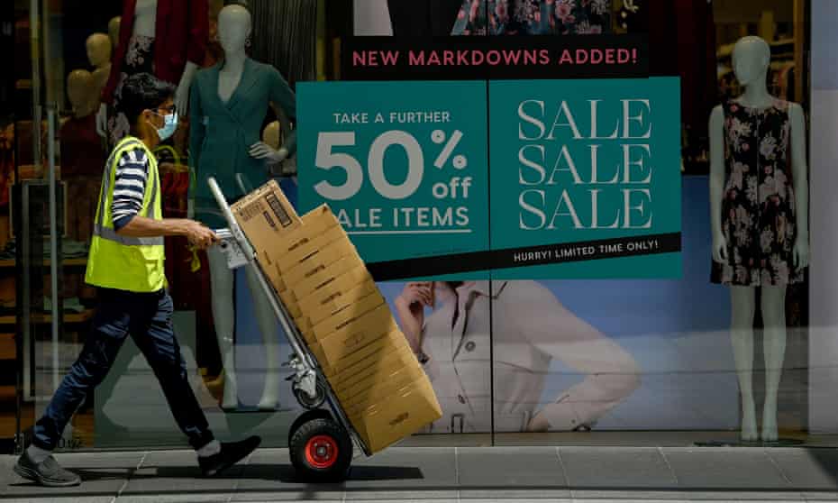 Masked worker transporting boxes past a 50% off sale sign in Sydney