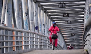 Una mujer con una máscara facial y un traje de bioseguridad monta su bicicleta mientras cruza un puente en Kennedy en Bogotá en julio.