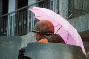 A US soldier from 8th Regiment, riding on top of an armoured personnel carrier, shelters beneath a pink umbrella in Saigon during the Mini-Tet offensive, 1968