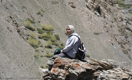 A young woman sits on a rocky outcrop on a mountain side.
